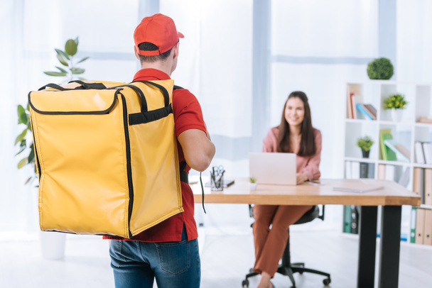 Back view of delivery man with thermo backpack and smiling businesswoman at table in office - Foto, Imagen
