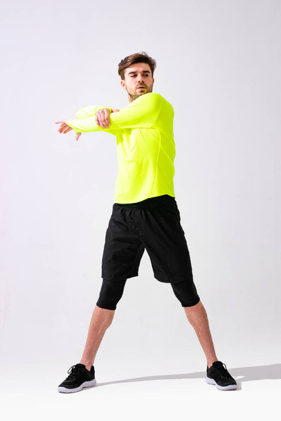 doing stretching first. young man in sportwear training and stretching his muscle on white background - Fotoğraf, Görsel