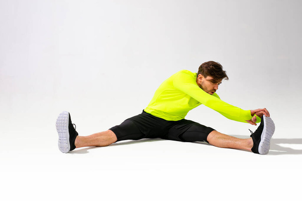 doing stretching first. young man in sportwear training and stretching his muscle on white background - Фото, изображение