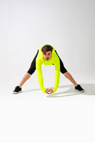 eerst aan het stretchen. jonge man in sportwear training en stretching zijn spier op witte achtergrond - Foto, afbeelding