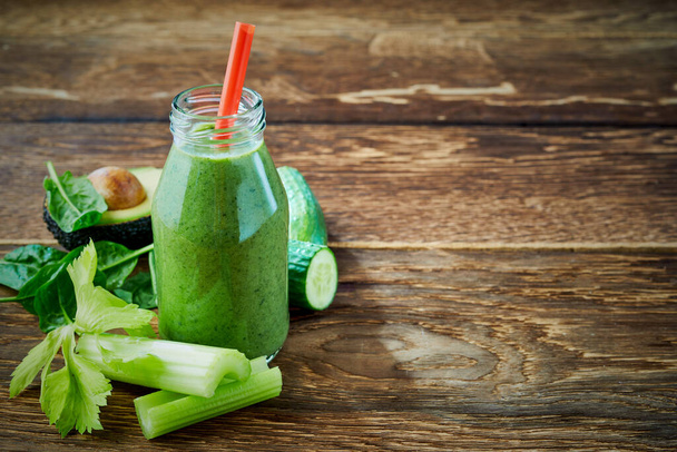 Zdravá zelená zelenina smoothie ve sklenici s čerstvými ingrediencemi vedle celeru, špenátu, avokáda hrušky a okurky na rustikálním dřevě pozadí s kopírovacím prostorem - Fotografie, Obrázek