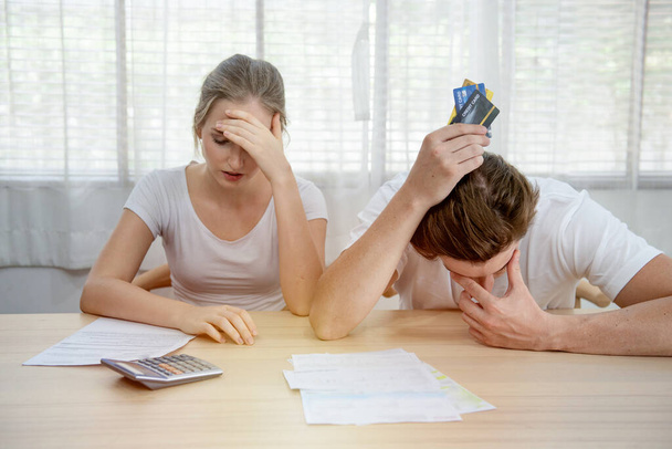Молодая кавказская пара, держащая кредитную карту и долговой счет на столе дома, мужчины и женщины имеют просроченные проблемы с финансовым залогом сидеть в комнате с серьезной и несчастливой оплаты
. - Фото, изображение