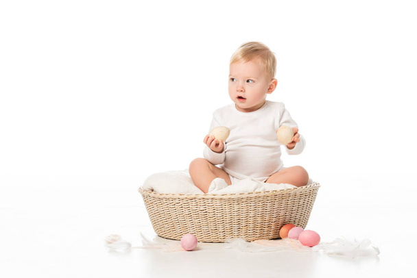 Kid holding easter eggs, looking away with open mouth, sitting in basket on white background - Photo, Image