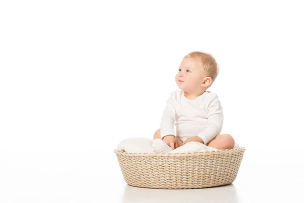 Cute child looking away and sitting on blanket in basket on white background - Φωτογραφία, εικόνα