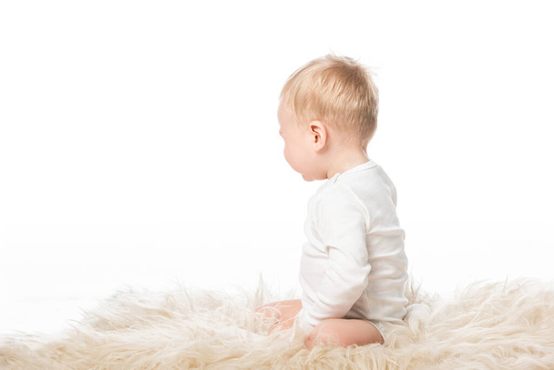 Seitenansicht von niedlichen Kind sitzt auf Fell isoliert auf weiß  - Foto, Bild