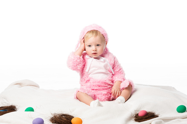 Upset child wearing rabbit costume, touching head on blanket with colorful decoration isolated on white  - Foto, imagen
