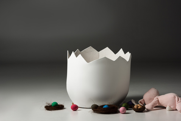 Guscio d'uovo vuoto accanto a nidi, uova di Pasqua e coniglietto su sfondo nero
 - Foto, immagini