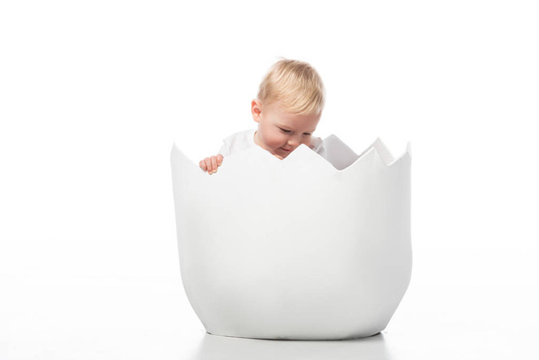 Criança bonito olhando para baixo dentro casca de ovo no fundo branco
 - Foto, Imagem
