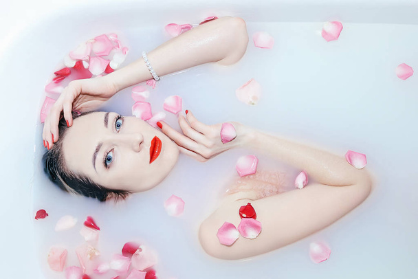 Joven chica sexy tomando un baño de leche con pétalos de rosa
 - Foto, Imagen