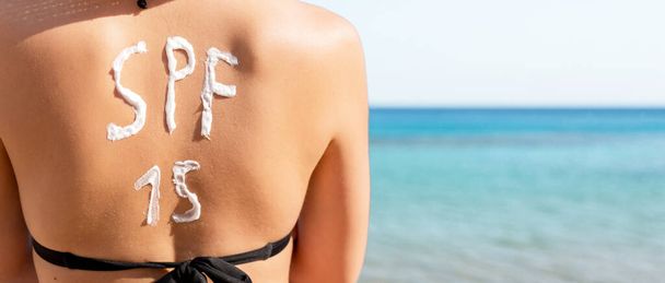 Pretty woman has spf 15 word made of sun cream on her back at th - Photo, Image