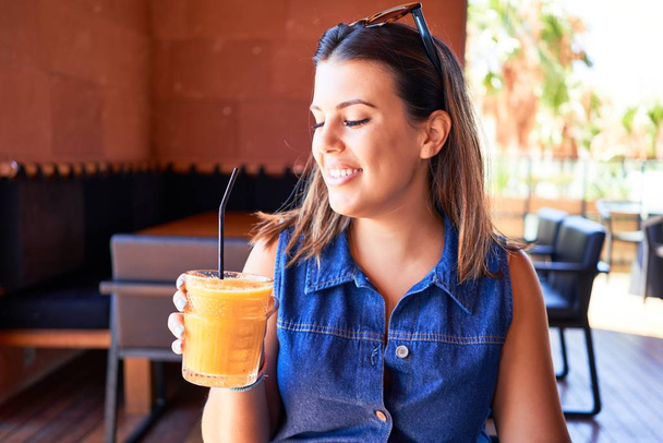 Young beautiful woman sitting at restaurant enjoying summer vacation drinking healthy smoothie - Foto, afbeelding