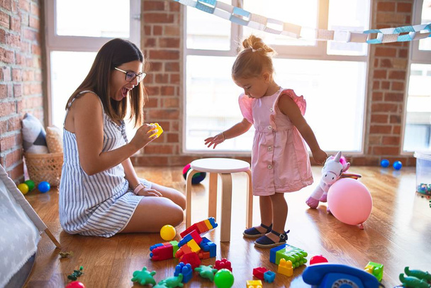 Jeune belle enseignante et tout-petit jouant avec des blocs de construction jouet sur la table à la maternelle
 - Photo, image