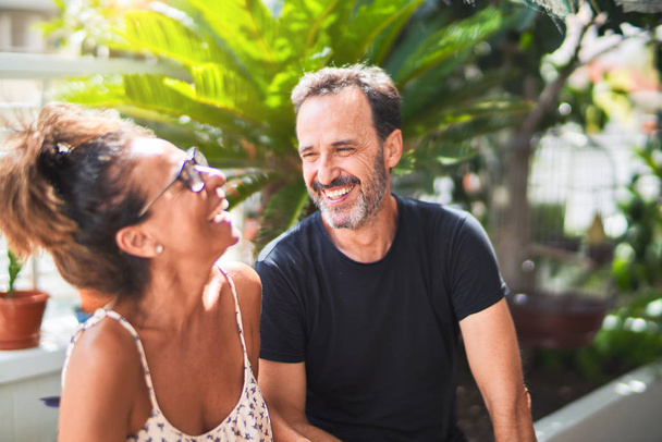 Schönes Paar mittleren Alters sitzt auf der Terrasse und spricht und lächelt - Foto, Bild