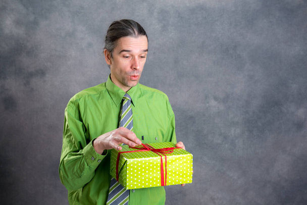 молодий чоловік в зеленій сорочці і краватка з зеленою подарунковою коробкою здивований
 - Фото, зображення
