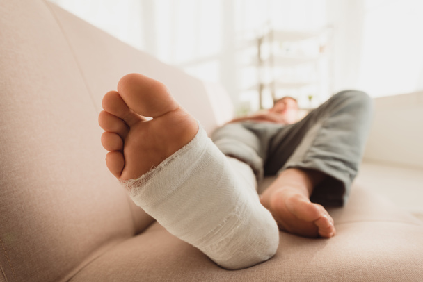 Selektywne skupienie człowieka ze złamaną nogą leżącego na kanapie - Zdjęcie, obraz