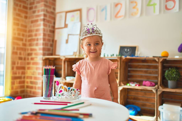 Beautiful blond toddler girl wearing princess crown standing at kindergarten - Photo, image