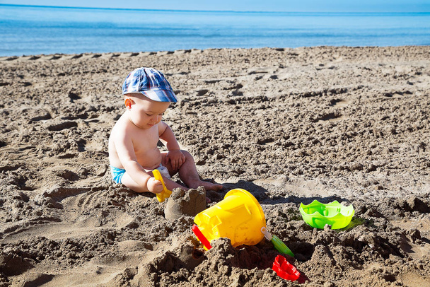 Child with with dad's hat playing with sand on beach on summer vacation. Travel and adventure concept. - Foto, Bild