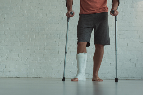 Cropped view of man with broken leg holding crutches  - Fotó, kép