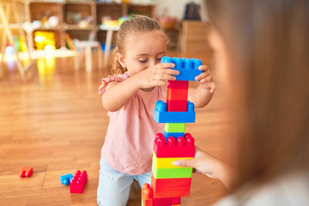 Belle enseignante et petite fille blonde construisant la tour en utilisant des blocs en plastique à la maternelle
 - Photo, image