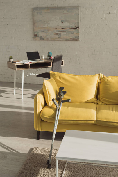 Sunlit living room with crutches near yellow sofa  - Foto, Imagem