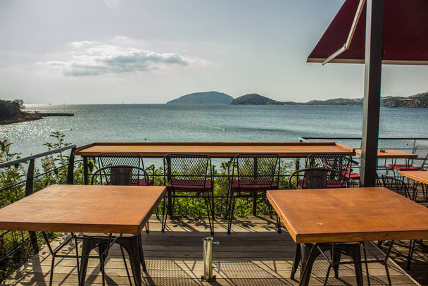 屋外パティオカフェ屋外デザインのバルコニースペース空の木製家具テーブルと海の近くの椅子南の自然景観 - 写真・画像