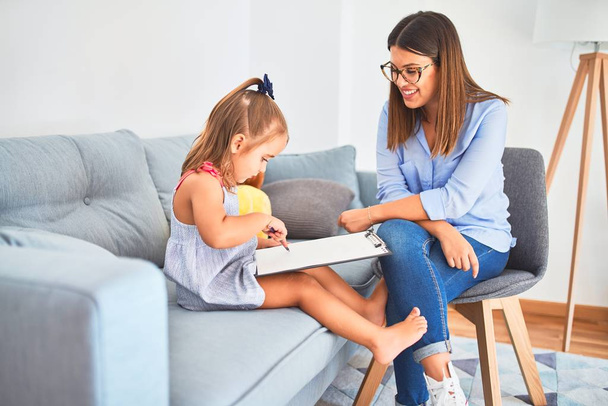 Young therapist woman speaking and treating child, counselor and behaviour correction at pedagogue payroom taking notes on clipboard - Foto, imagen