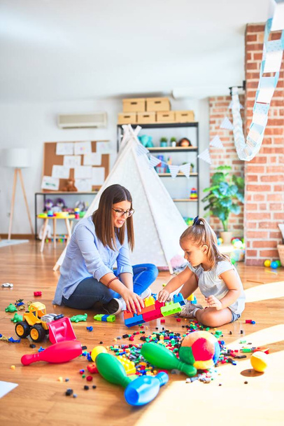 Caucasian girl kid playing and learning at playschool with female teacher. Mother and daughter at playroom around toys playing with bulding blocks - Фото, зображення