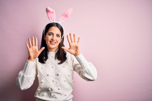 Young caucasian woman wearing cute easter rabbit ears over pink isolated background showing and pointing up with fingers number ten while smiling confident and happy. - Fotografie, Obrázek