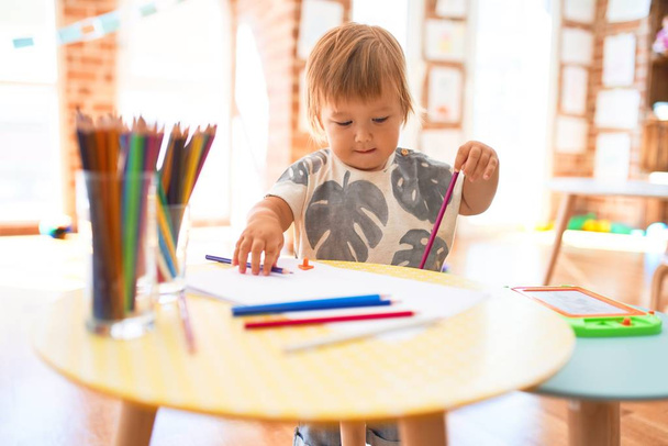 Adorable toddler drawing using paper and pencil around lots of toys at kindergarten - Photo, Image