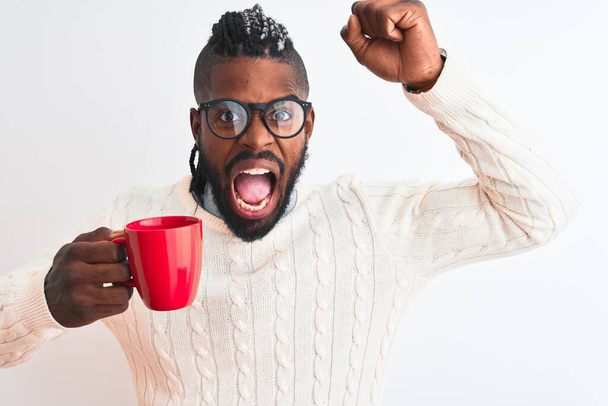 Afrykański Amerykanin z warkoczami pijący kawę na odizolowanym białym tle zirytowany i sfrustrowany krzykiem ze złości, szalony i wrzeszczący z podniesionymi rękami, koncepcja złości - Zdjęcie, obraz