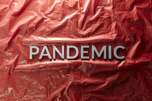 das Wort Pandemie mit silbernen Buchstaben auf rotem zerknittertem Kunststofffolienhintergrund in flacher Lagezusammensetzung in der Mitte - Foto, Bild