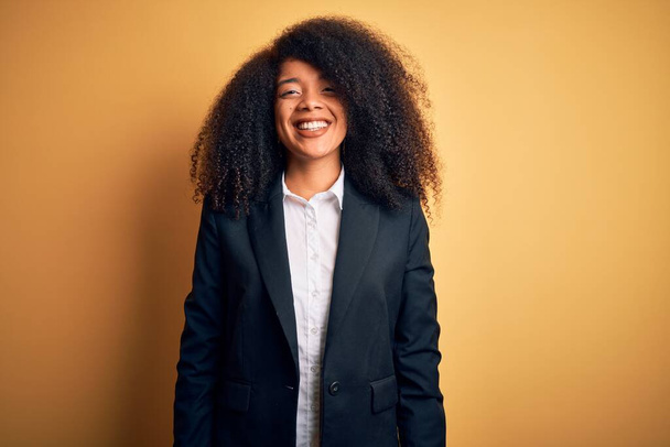 Νεαρή όμορφη αφροαμερικανίδα επιχειρηματίας με αφρο μαλλιά που φοράει κομψό σακάκι με χαρούμενο και δροσερό χαμόγελο στο πρόσωπο. Τυχερός άνθρωπος. - Φωτογραφία, εικόνα