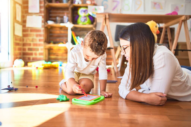 Красивий вчитель і малюк малюють за допомогою цифрової дошки навколо безлічі іграшок в дитячому саду
 - Фото, зображення
