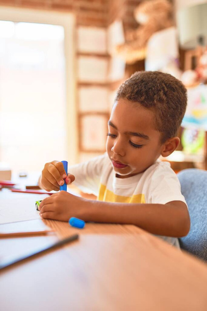 Beautiful african american toddler sitting painting car toy using marker pen on desk at kindergarten - Foto, imagen
