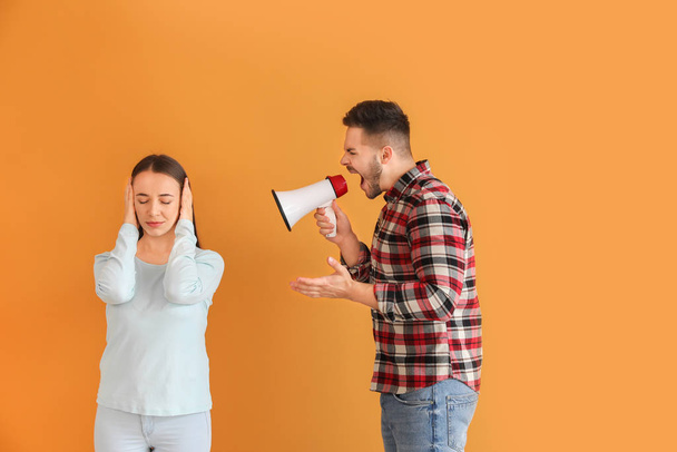 Angry man with megaphone shouting at his wife on color background - Foto, imagen