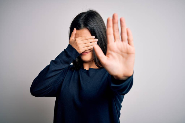Young beautiful brunette woman wearing casual sweater standing over white background covering eyes with hands and doing stop gesture with sad and fear expression. Embarrassed and negative concept. - Foto, Imagem