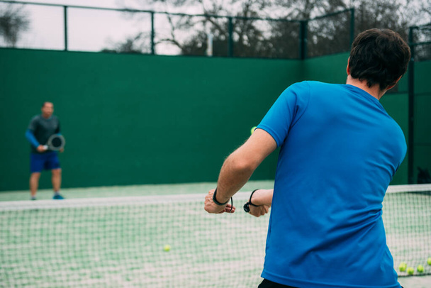 Young man playing paddle tennis on a green court, wearing a blueYoung man playing paddle tennis on a green court, wearing a blue t-shirt.Sports concept.Copy space - Foto, Imagem