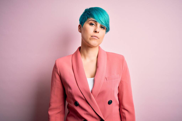 Young beautiful businesswoman with blue fashion hair wearing jacket over pink background Relaxed with serious expression on face. Simple and natural looking at the camera. - 写真・画像