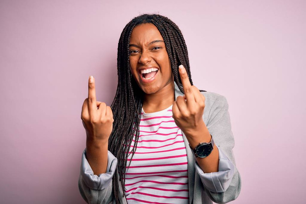 Молодая африканская деловая женщина, стоящая на розовом изолированном фоне, показывает средний палец, делающий трахнуть вас плохое выражение лица, провокация и грубое отношение. Крики возбуждения
 - Фото, изображение