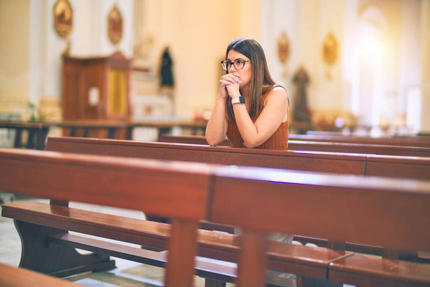Nuori kaunis nainen rukoilee polvillaan penkillä kirkossa
 - Valokuva, kuva