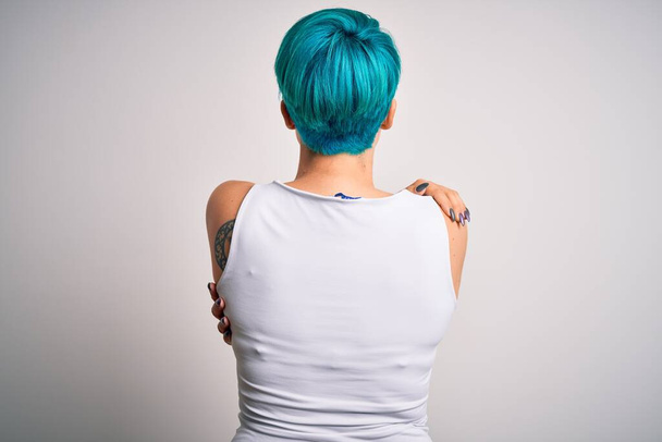 Jeune belle femme avec des cheveux de mode bleus portant un t-shirt décontracté sur fond blanc S'embrasser heureux et positif à partir de l'arrière. Amour de soi et soin de soi
 - Photo, image