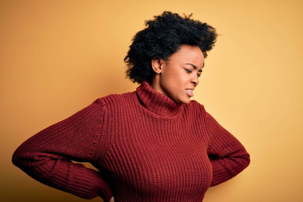 Young beautiful African American afro woman with curly hair wearing casual turtleneck sweater Suffering of backache, touching back with hand, muscular pain - Foto, Imagem