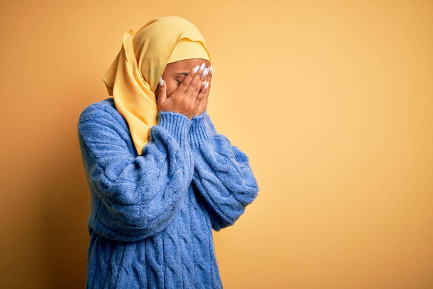 Young African American afro woman wearing muslim hijab over isolated yellow background with sad expression covering face with hands while crying. Depression concept. - Fotó, kép