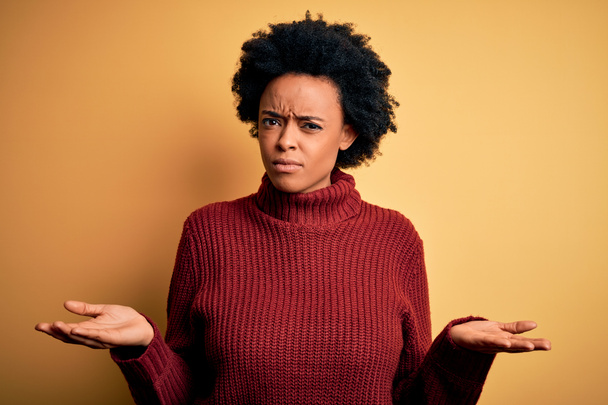 junge schöne afrikanisch-amerikanische Afro-Frau mit lockigem Haar trägt lässigen Rollkragenpullover ahnungslos und verwirrt mit offenen Armen, keine Ahnung Konzept. - Foto, Bild