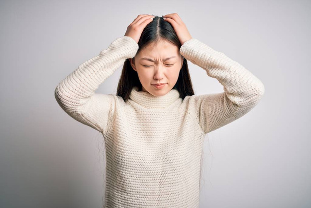 Young beautiful asian woman wearing casual sweater standing over isolated background suffering from headache desperate and stressed because pain and migraine. Hands on head. - Zdjęcie, obraz