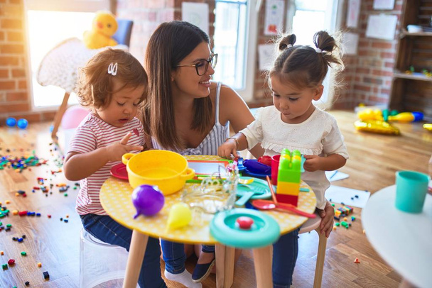 Jovem e bela professora e crianças jogando refeições usando alimentos de plástico e brinquedo de talheres no jardim de infância
 - Foto, Imagem