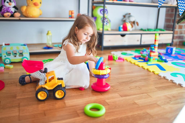 entzückendes blondes Kleinkind baut Pyramide mit Reifen um jede Menge Spielzeug im Kindergarten - Foto, Bild