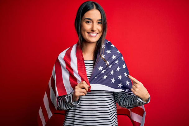 Молодая красивая брюнетка патриотическая женщина, носящая флаг США на день независимости очень счастливо указывая рукой и пальцем
 - Фото, изображение