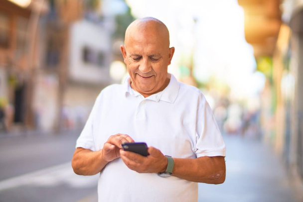 Senior gutaussehender Mann lächelt glücklich und zuversichtlich. Mit Smartphone lächelnd an der Stadtstraße stehen - Foto, Bild