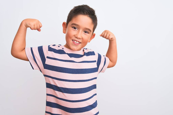Mooie jongen draagt casual gestreepte t-shirt staan over geïsoleerde witte achtergrond tonen armen spieren glimlachen trots. Fitness concept. - Foto, afbeelding